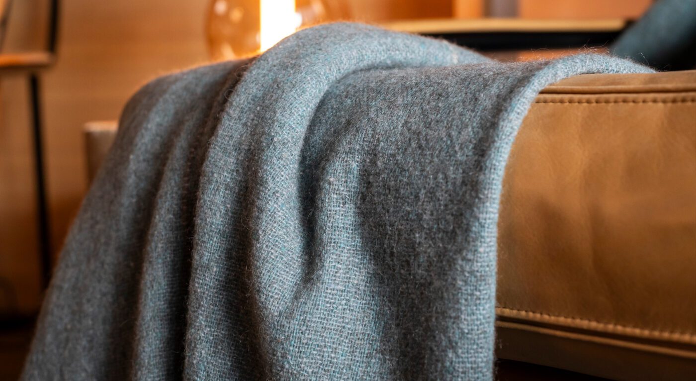 A Nomad throw in grey color, made from merino wool and yak, resting on a sofa