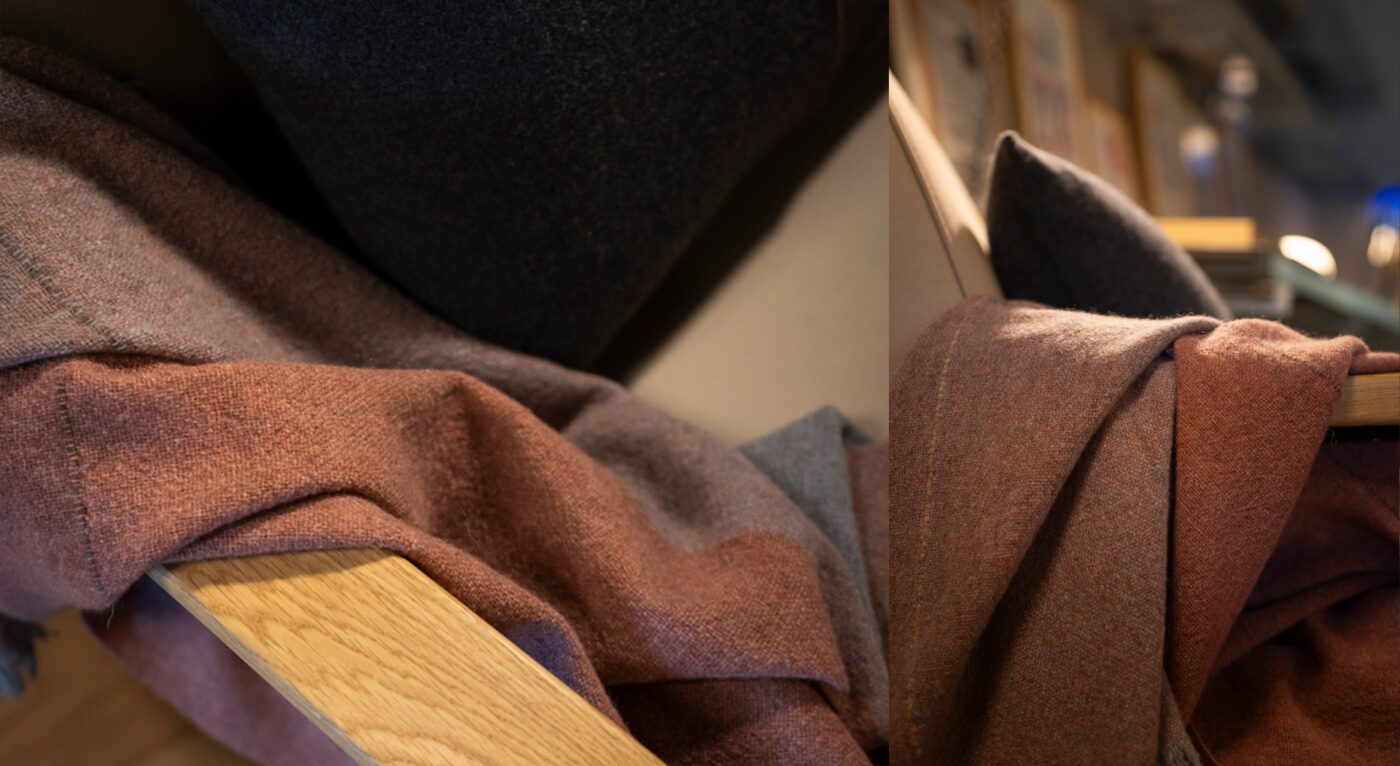 A Nomad throw in copper color, made from merino wool and yak, resting on a chair.